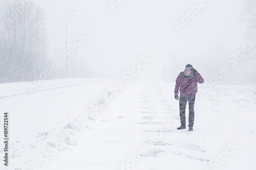 Winter is coming by snow. Poor visibility in heavy snow storm on path. Man slowly and hard walking in dangerous weather day. Cataclysm of nature. City people life in blizzard concept.