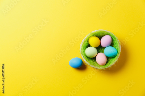 Six colorful pastel monophonic painted Easter eggs in basket with green grass isolated on yellow background. Happy Easter concept. Copy space for advertisement. With place for text. Top view on eggs.