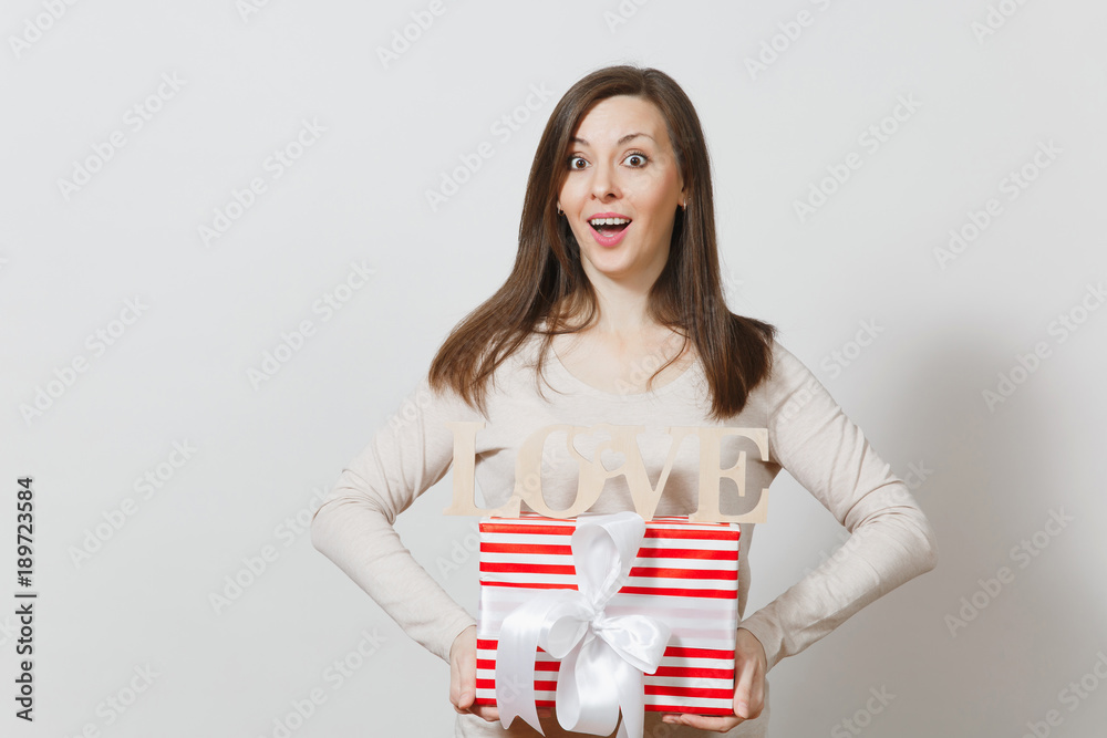 Beautiful young sexy smiling woman holding red present box with gift, wooden word love on white background. Copy space for advertisement. St. Valentine's Day or International Women's Day concept. Beautiful young sexy smiling woman holding red present box with gift, wooden word love on white background. Copy space for advertisement. St. Valentine's Day or International Women's Day concept.