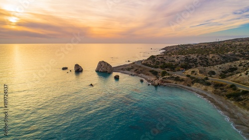Aerial Bird's eye view of Petra tou Romiou, aka Aphrodite's rock a famous tourist travel destination landmark in Paphos, Cyprus. The sea bay of goddess Afroditi birthplace at sunset from above. photo
