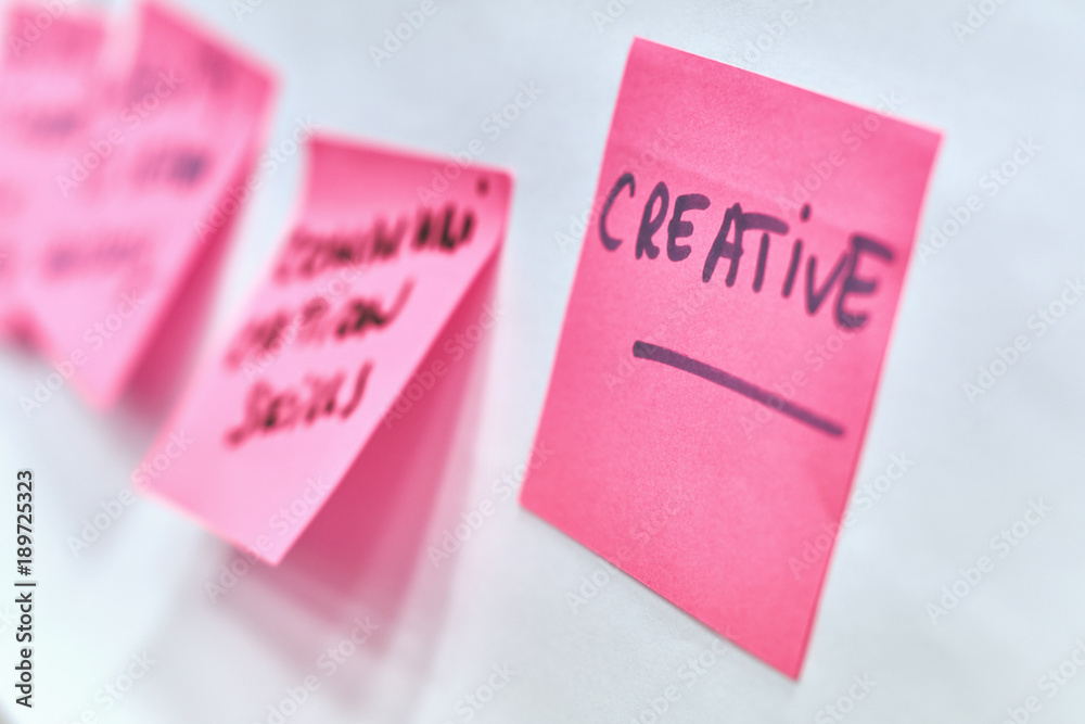 Creative written on pink and yellow paper stickers attached to a flip chart on a whiteboard