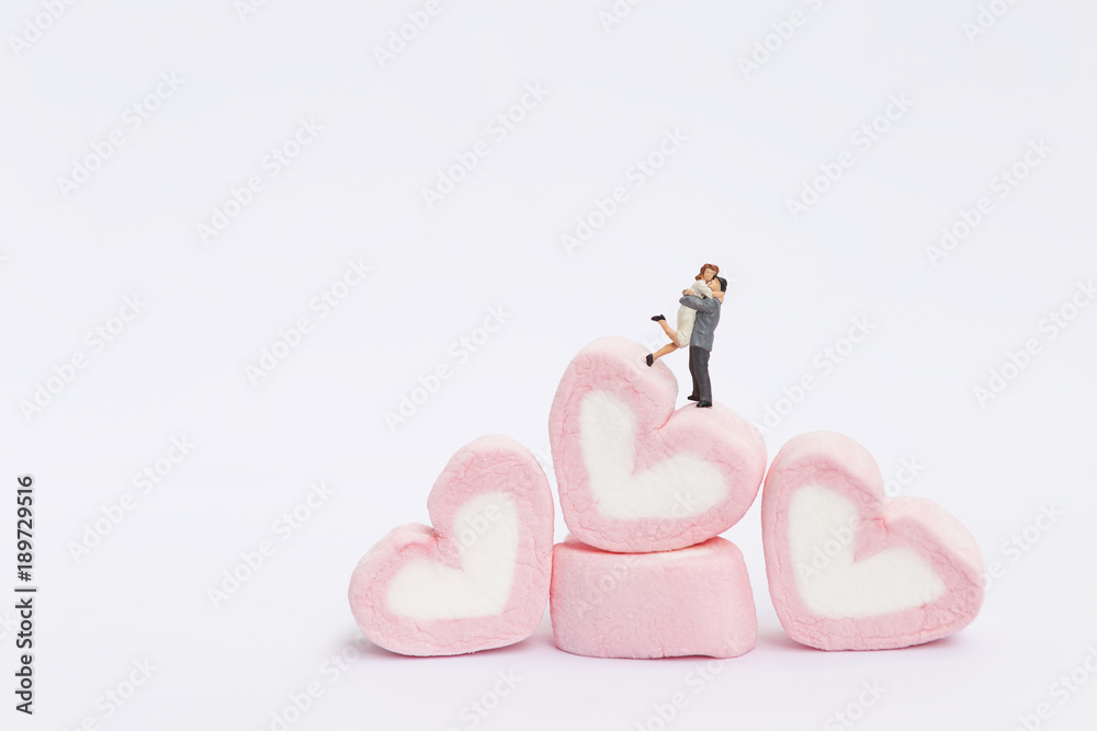 Fototapeta premium Happy miniature couple on stack on pink heart marshmallow on white background, valentine concept background