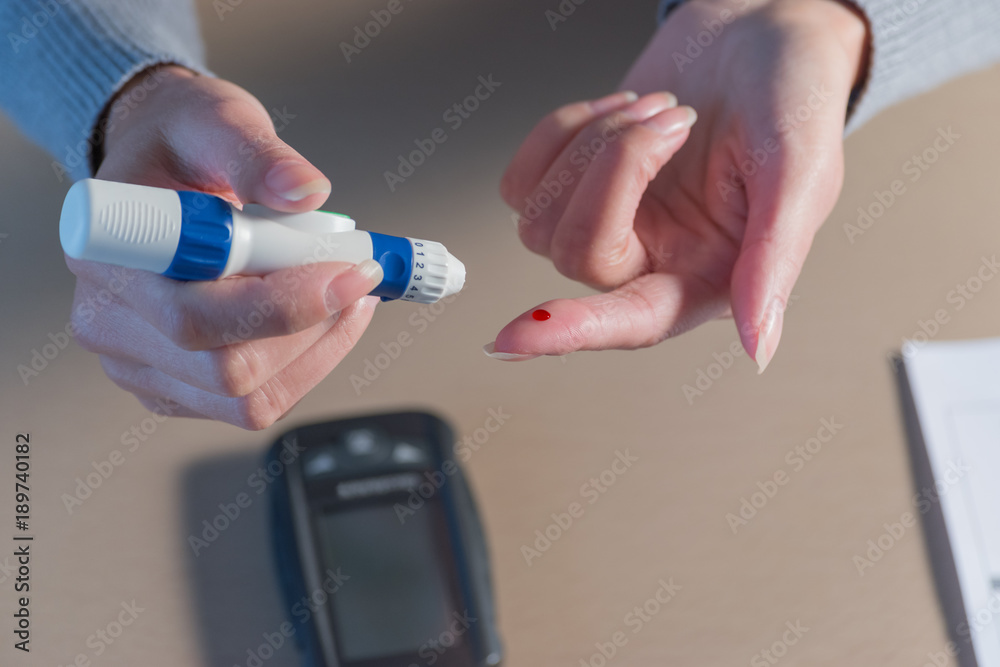 Close-up of woman hands using lancet on finger to check blood sugar level by Glucose meter. Health care concept.