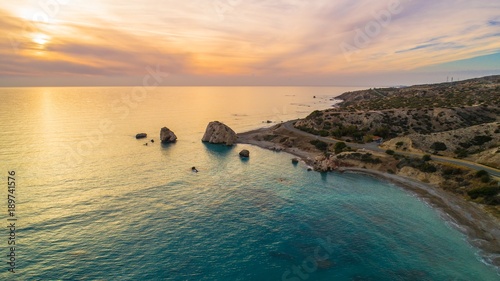     Aerial Bird's eye view of Petra tou Romiou, aka Aphrodite's rock a famous tourist travel destination landmark in Paphos, Cyprus. The sea bay of goddess Afroditi birthplace at sunset from above.  photo