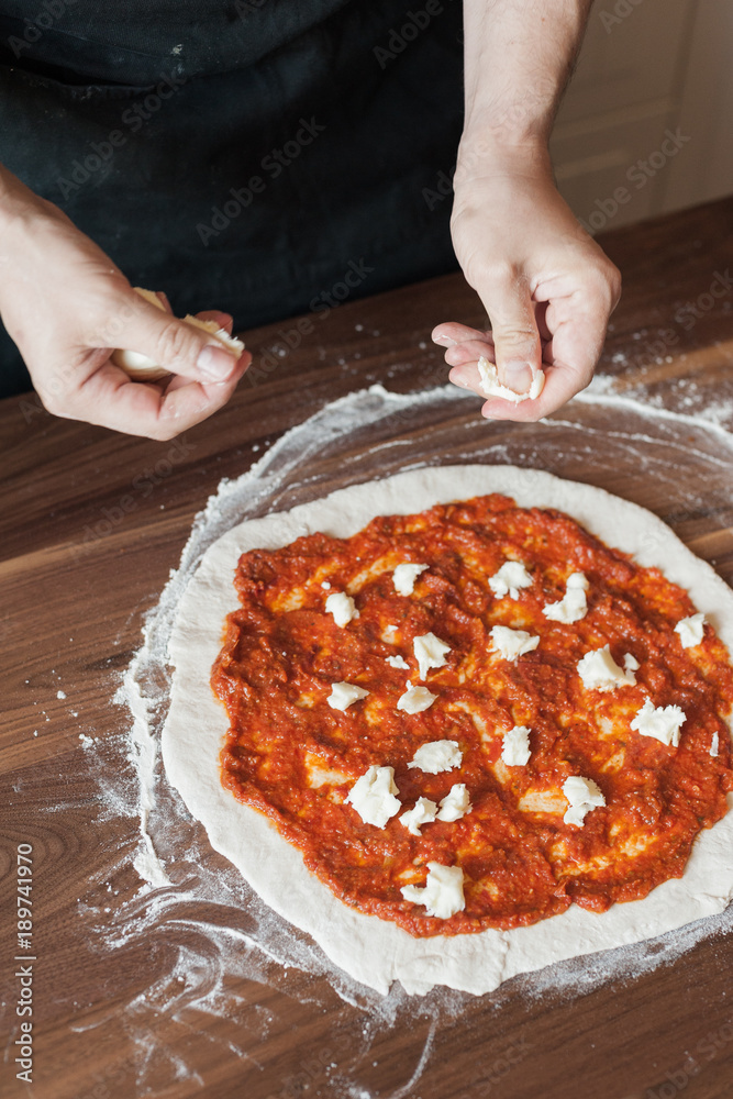 A man is cooking pizza. Arms puts cheese on dough with tomato paste