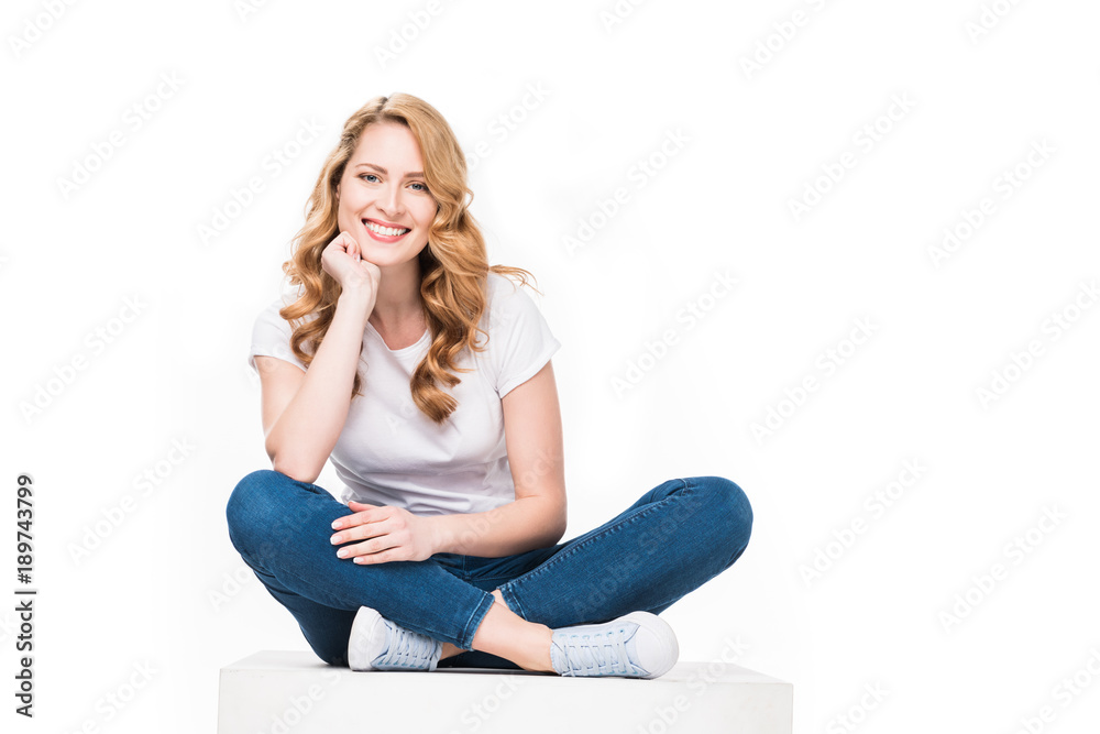 smiling woman sitting on white cube isolated on white