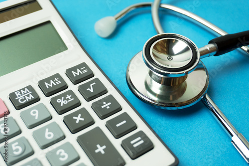 Close up of calculator and stethoscope on blue background - Business and Insurance concept