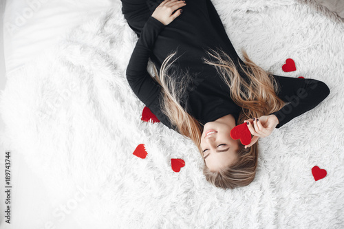 Young beautiful woman with a nice smile,a blonde with long straight hair,spends time alone in the big bright room,holding hands of little Krasnye the heart is a symbol of Valentine's day photo