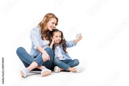 happy mother and daughter taking selfie on smartphone together isolated on white