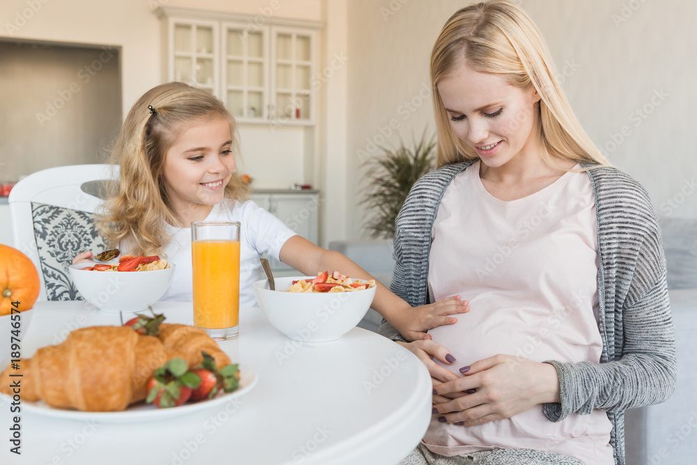 smiling daughter touching pregnant mother belly