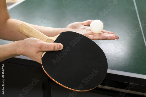 Training on table tennis.
A woman is putting a tennis ball into the game.Tennis racket and ball on the background of the green game table.