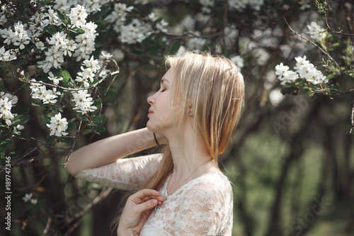 Spring beautiful romantic girl, blonde, enjoying blooming apple trees in swarn sunny day photo