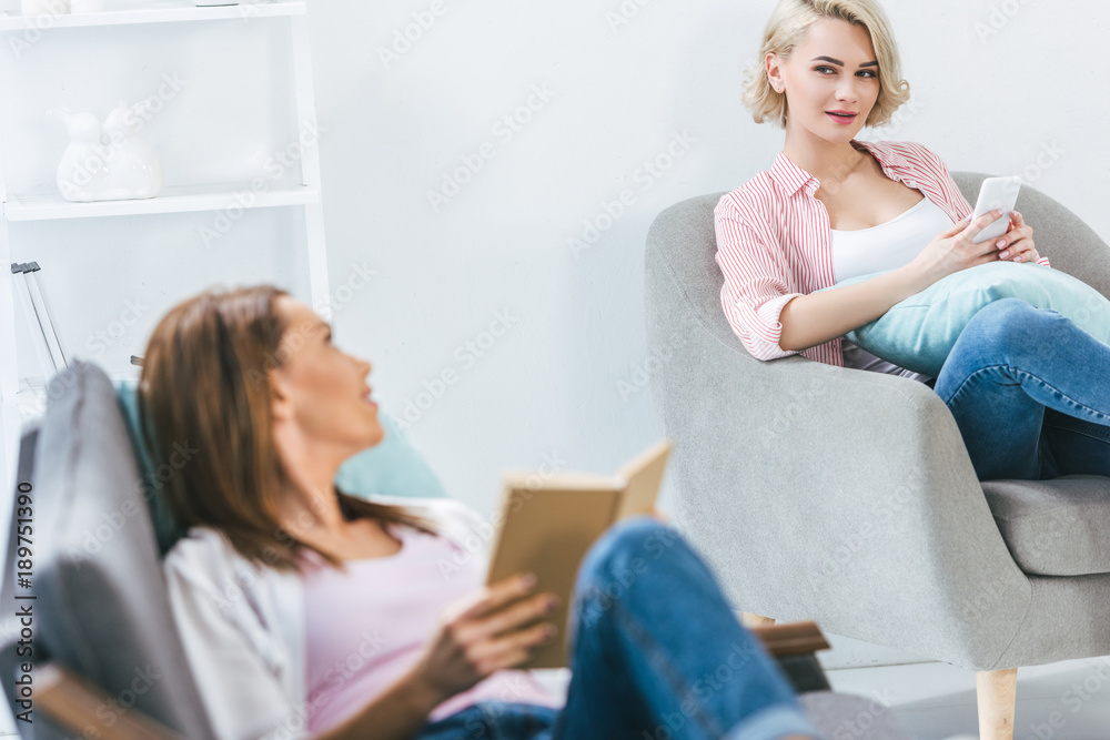 female friends reading book and using smartphone at home female friends reading book and using smartphone at home