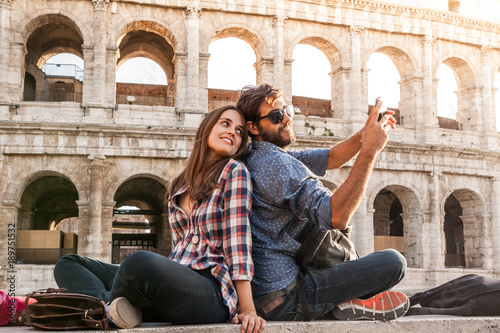 Photography Happy couple sitting in front of colosseum in rome taking selfie pictures with smartphone camera