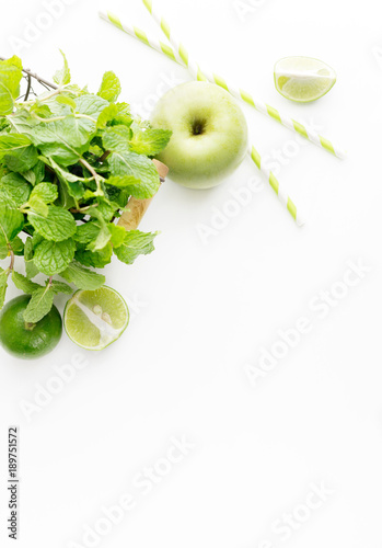 Green healthy drink ingredients on white background: lime, apple, fresh mint and colorful paper straws. Vegetarian food. Detox. Text space