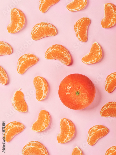 Whole tangerine surrounded by tangerine pieces isolated on hot pink background. Copy space. Flat lay. Healthy eating