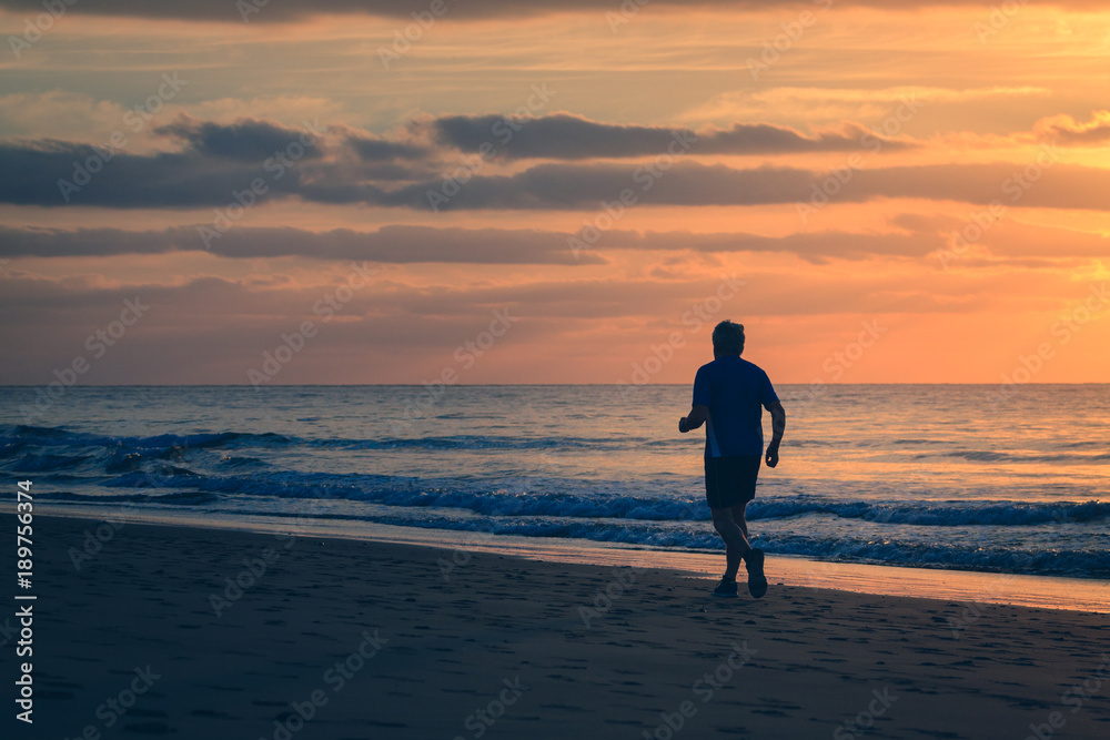 Man is running by the beach at sunrise.