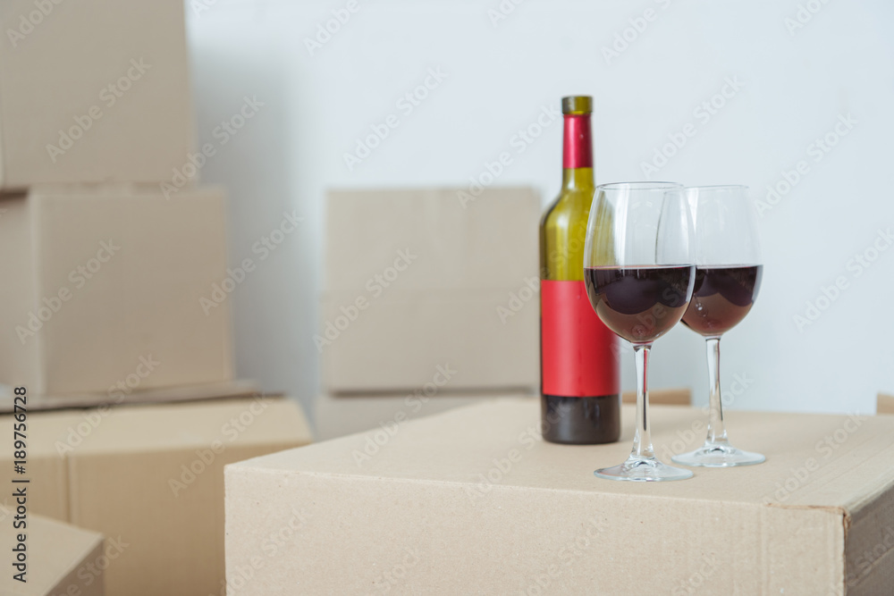 close-up view of bottle and glasses with wine on cardboard box during relocation
