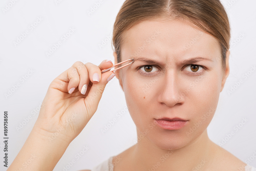 Woman plucking eyebrows with tweezers over grey background. Woman plucking eyebrows with tweezers over grey background.