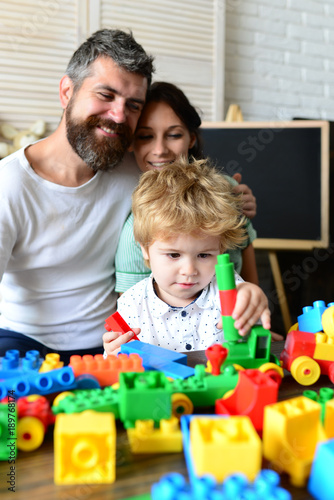 Parents watch their son with happy faces making brick constructions.