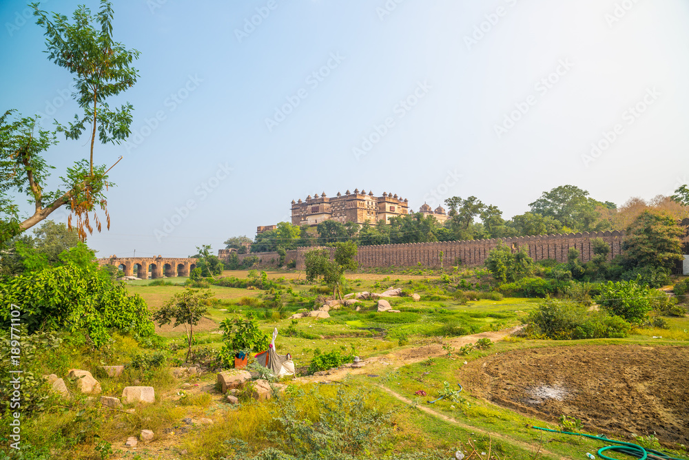 Naklejka premium Orchha Palace, sunny day and blue sky, green landscape and cultivated fields around. Also spelled Orcha, famous travel destination in India.