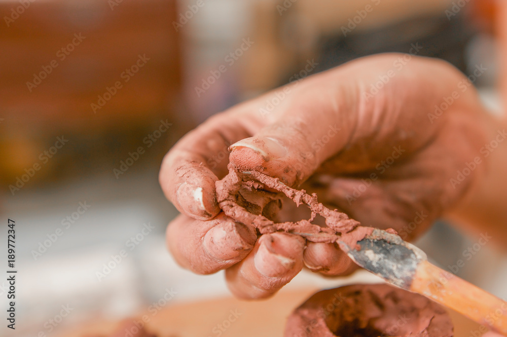 Close up of woman ceramist hands cleanning the tool after working on sculpture on wooden table in workshop, in a blurred background