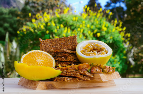 Outdoor view of granola bars with cereals over a wooden table, orange and passion fruit on blurred nature background photo