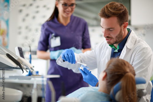 Dentist showing properly brushing teeth to girl in ambulant