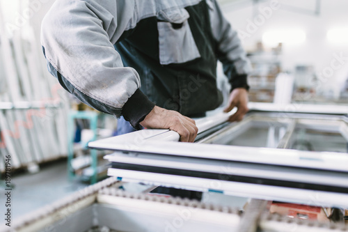 Factory for aluminum and PVC windows and doors production. Manual worker assembling PVC doors and windows. Selective focus. 