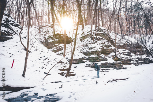 The sunlight shining through the woods as a hiker in the distance treks through the snow covered ravine path in Utica, Illinois at Matthiessen State Park. photo