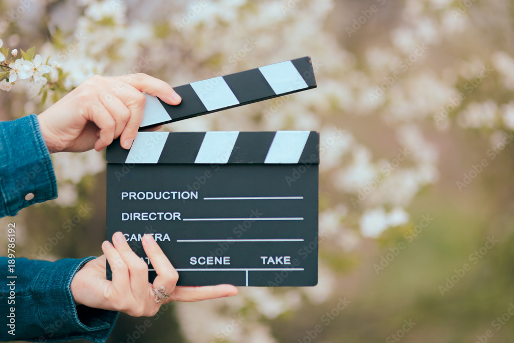 Fototapeta premium Hands Holding Film Slate Cinema Clapper on Spring Blooming Background