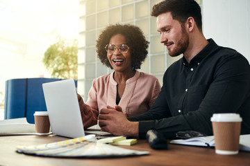 Two smiling businesspeople sitting in an office using a laptop