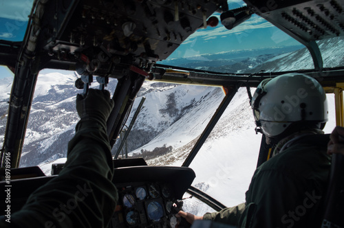 Military helicopter flying through white snowed mountains, pilot and copilot wearing green flightsuit and helmet view
