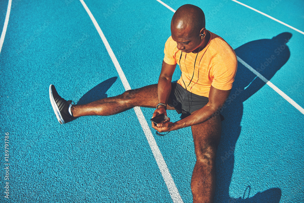 Fototapeta Young athlete sitting on a running track listening to music