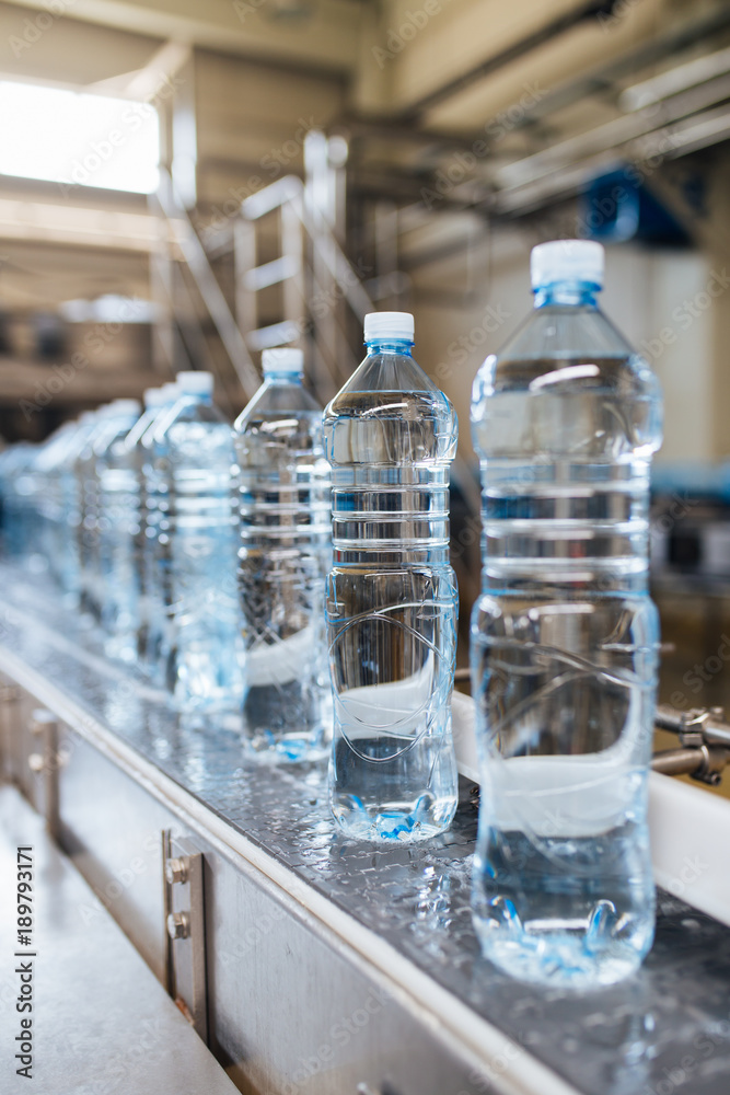 Bottling plant - Water bottling line for processing and bottling pure spring water into blue bottles. Selective focus. Bottling plant - Water bottling line for processing and bottling pure spring water into blue bottles. Selective focus.