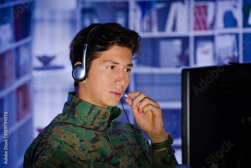 Portrait of handsome young soldier wearing a military uniform, military drone operator watching at his computer and using his headphone to give an advice photo