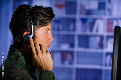 Portrait of handsome soldier wearing a military uniform watching important information in his computer, with one hand in the headphones and giving an advice in a blurred background, profile picture photo