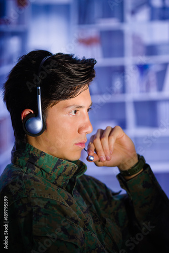 Portrait of a serious handsome man soldier wearing a military uniform watching important information in his computer, with one hand in the headphones in a blurred background, profile picture photo