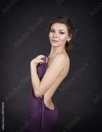 A young,smiling girl in dress posing on a dark background.