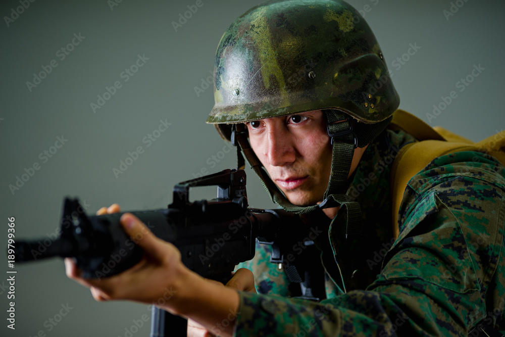 Portrait of young soldier holding in his hands a rifle, wearing a military uniform, in a gray background