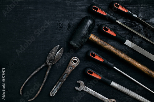 Series of many sharp steel blades and hammer on black wooden background photo