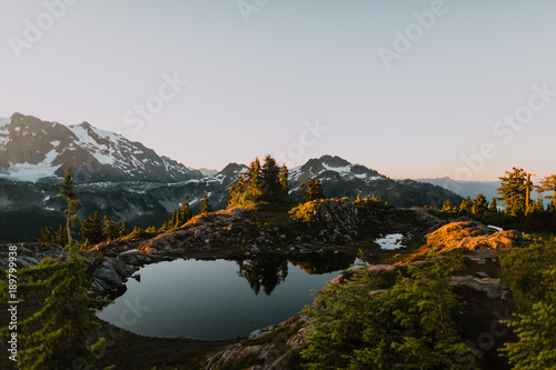 trees and mountain reflect in still pond at sunrise