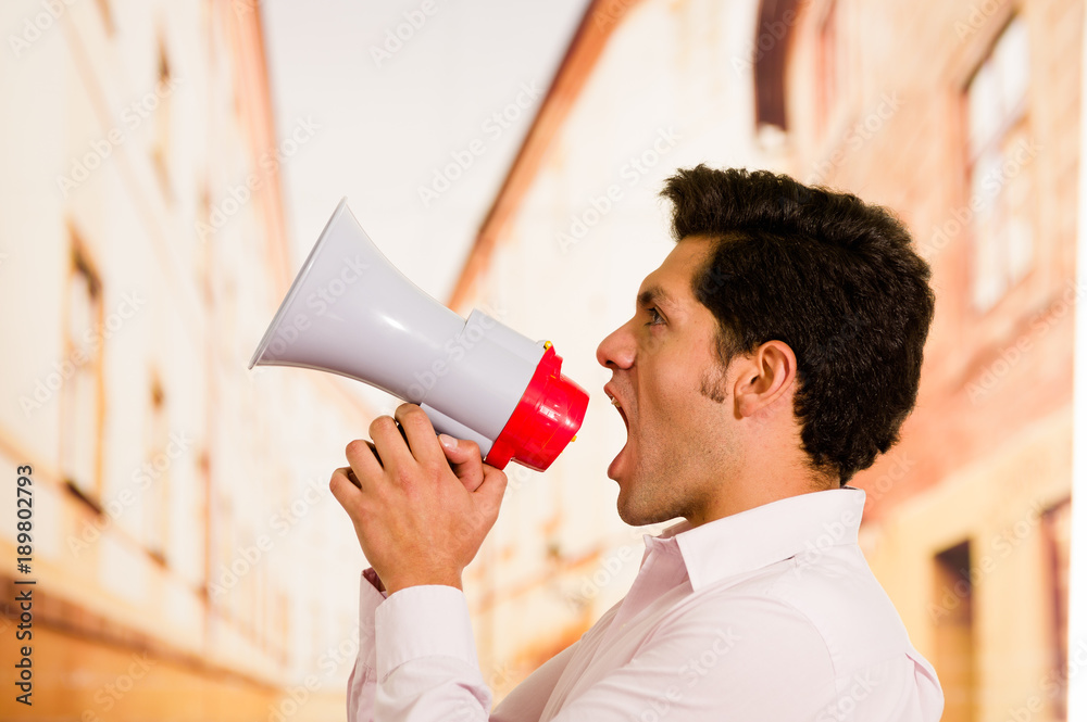 Close up of a handsome man screaming with a megaphone in a blurred background