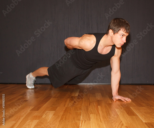 young fit caucasian male doing static exercise - plank on one hand