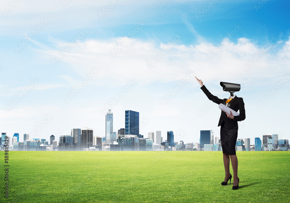 Camera headed woman standing on green grass against modern cityscape