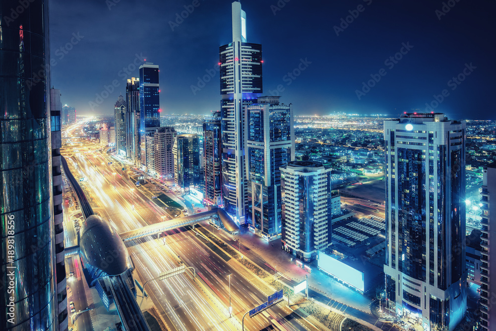 Fototapeta premium Aerial view of big highway interchange with traffic in Dubai, UAE, at night. Scenic cityscape. Colorful transportation, communications and driving background.