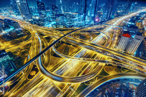 Aerial view of big highway interchange with traffic in Dubai, UAE, at night. Scenic cityscape. Colorful transportation, communications and driving background.