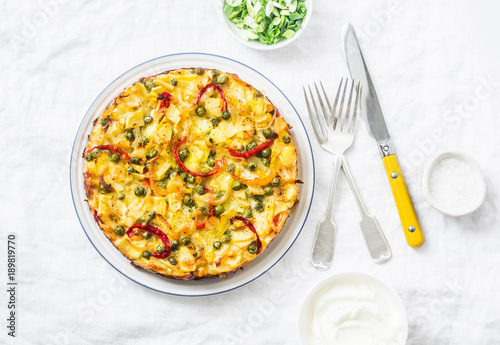 Potatoes and vegetables tortilla on a light background, top view. Potatoes, green beans, bell peppers, green peas, cheese, eggs casserole - a delicious breakfast or snack