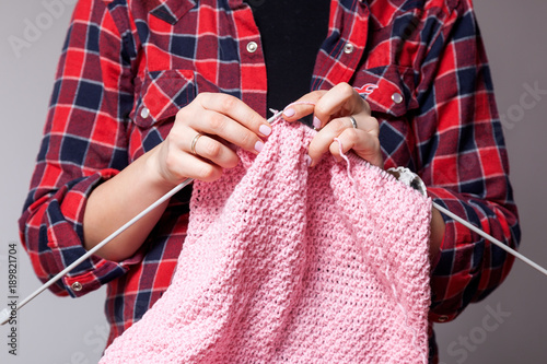 Close-up of a young woman in a plaid shirt knits with a knitted sweater of natural pink woolen yarns