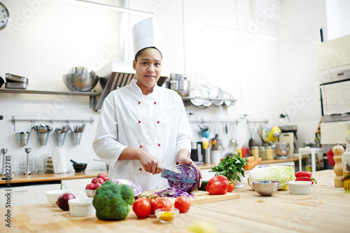 Young woman in chef uniform cooking fresh vegetable salad while cutting purple cabbage